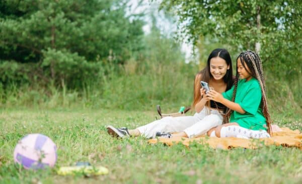 Two girls on a blanket smiling and looking into a cell phone